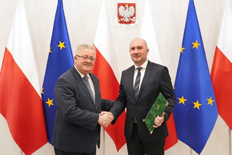 Minister Czesław Siekierski gratuluje Dr Maciejowi Gogulskiemu, w tle falki Polski oraz Unii Europejskiej  