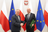 Minister Czesław Siekierski gratuluje Dr Maciejowi Gogulskiemu, w tle falki Polski oraz Unii Europejskiej  